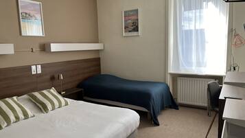 A hotel room with two beds, a desk, and a window with sheer curtains.