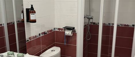 Un baño con lavamanos blanco, inodoro y ducha con mampara de vidrio.