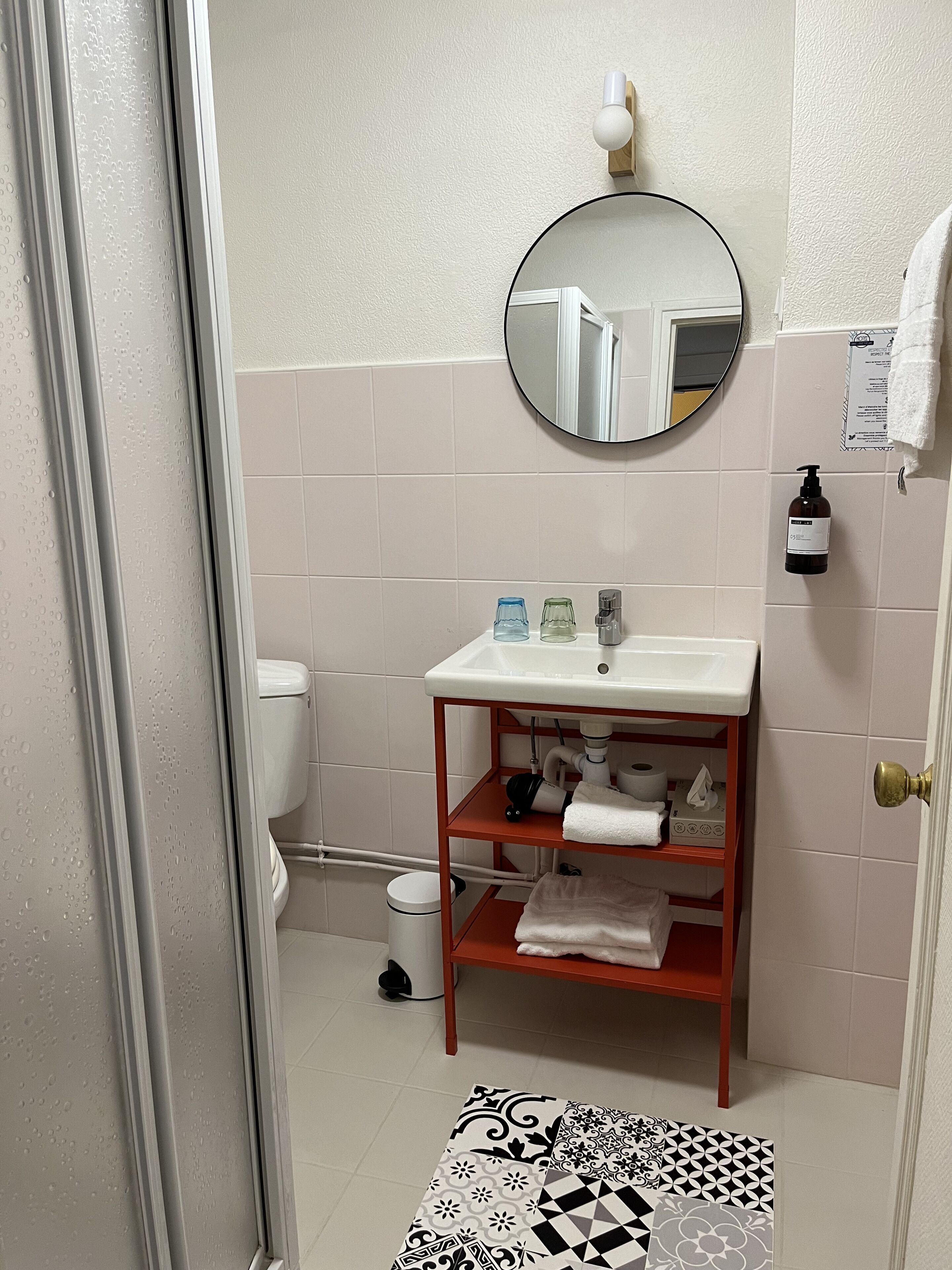 A bathroom with a white sink, a mirror, and a toilet. There is a towel rack on the wall and a shelf with towels and toiletries.