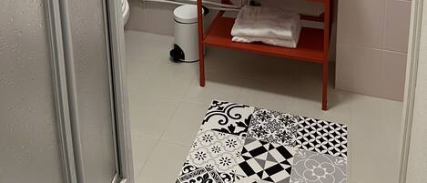 A bathroom with a white sink, a mirror, and a toilet. There is a towel rack on the wall and a shelf with towels and toiletries.