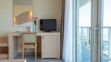 Una camera d'albergo moderna con una scrivania, una sedia, TV e vista sulla città attraverso ampie finestre.
