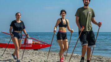 Tre persone che camminano su una spiaggia, con una barca rossa sullo sfondo.