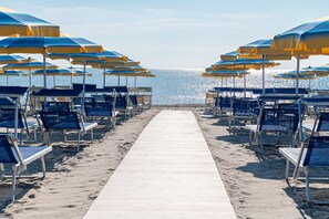 A beach with rows of blue and yellow beach chairs and umbrellas, a white walkway leading to the water. - Adria (Cervia)