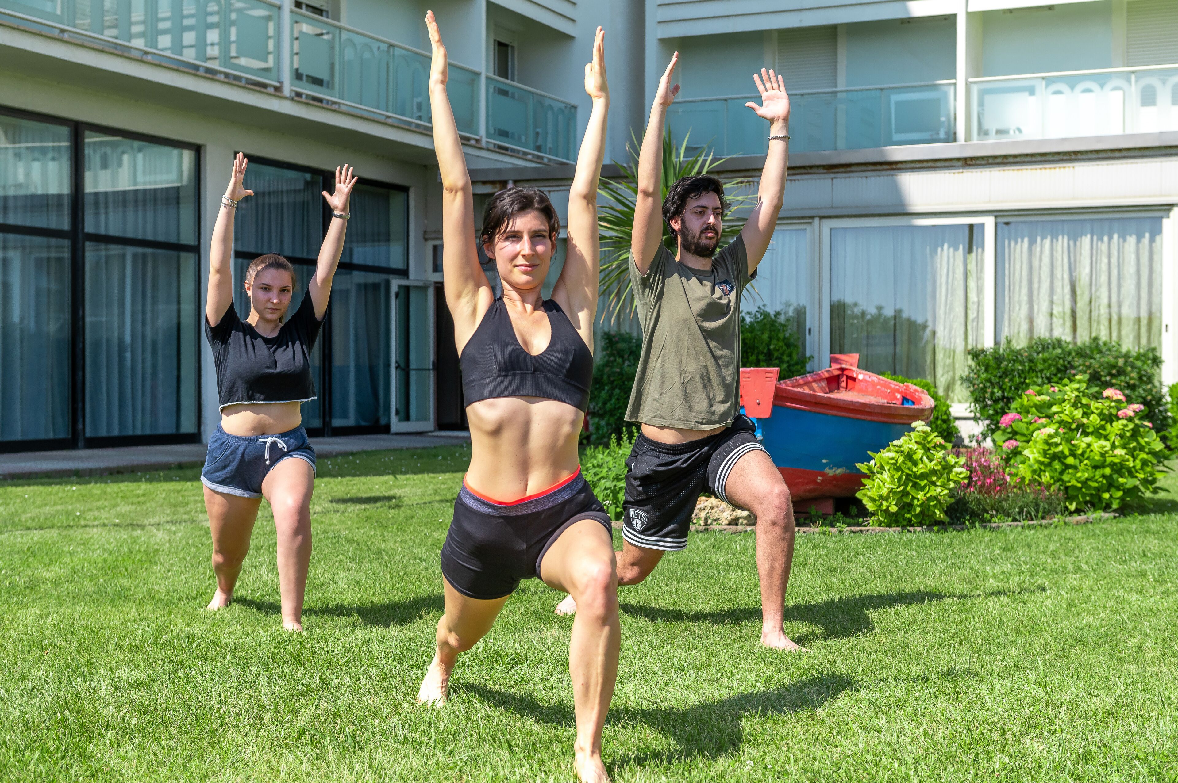 Tres personas realizando un ejercicio de sentadilla al aire libre, con un edificio y un barco en el fondo.