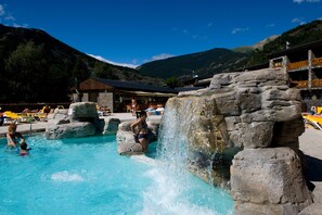 A pool area with a waterfall feature, surrounded by lounge chairs and a mountain backdrop. - Apartaments Giberga (La Massana)