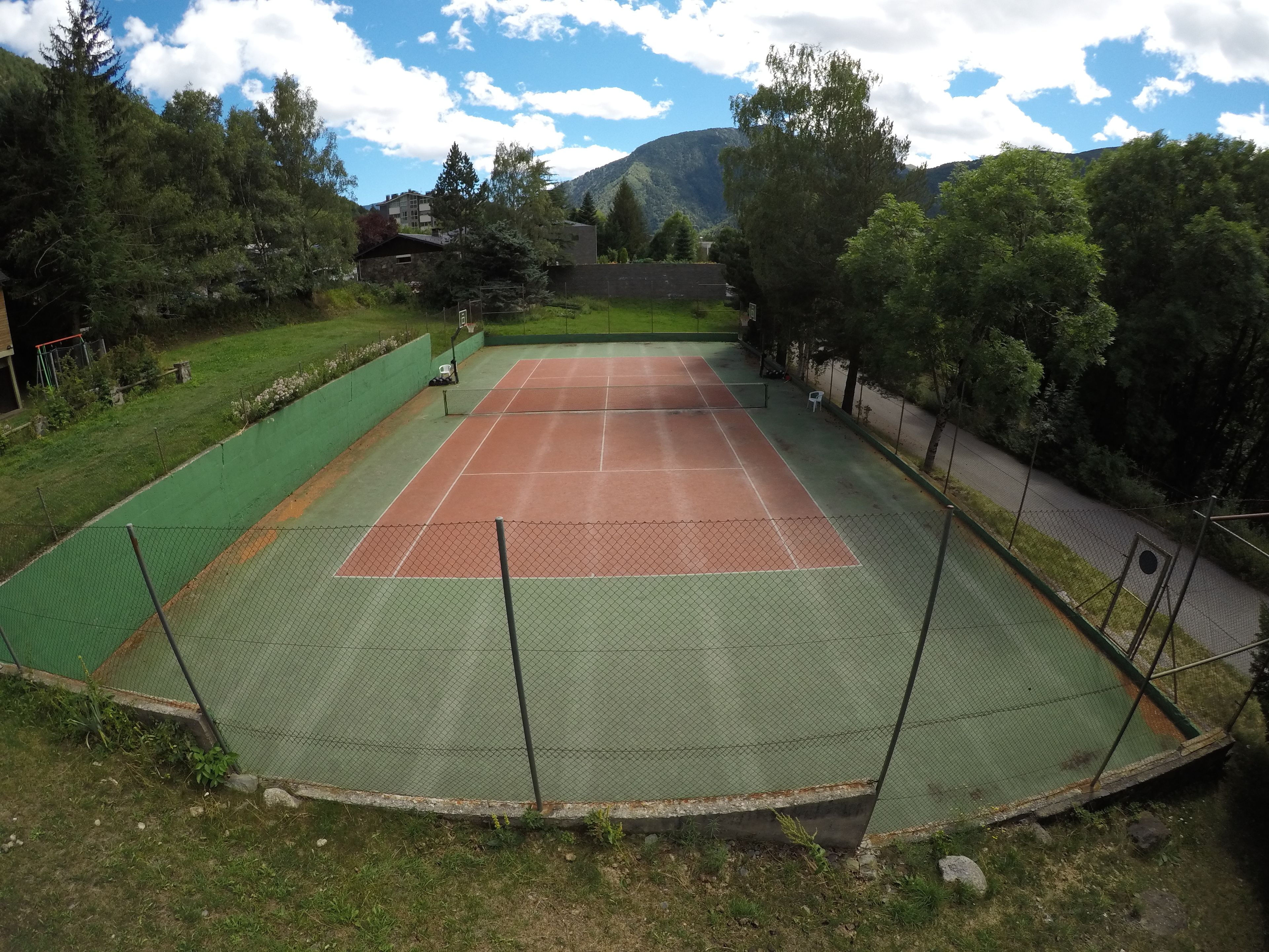 Un campo da tennis all'aperto circondato da vegetazione e con una montagna sullo sfondo.