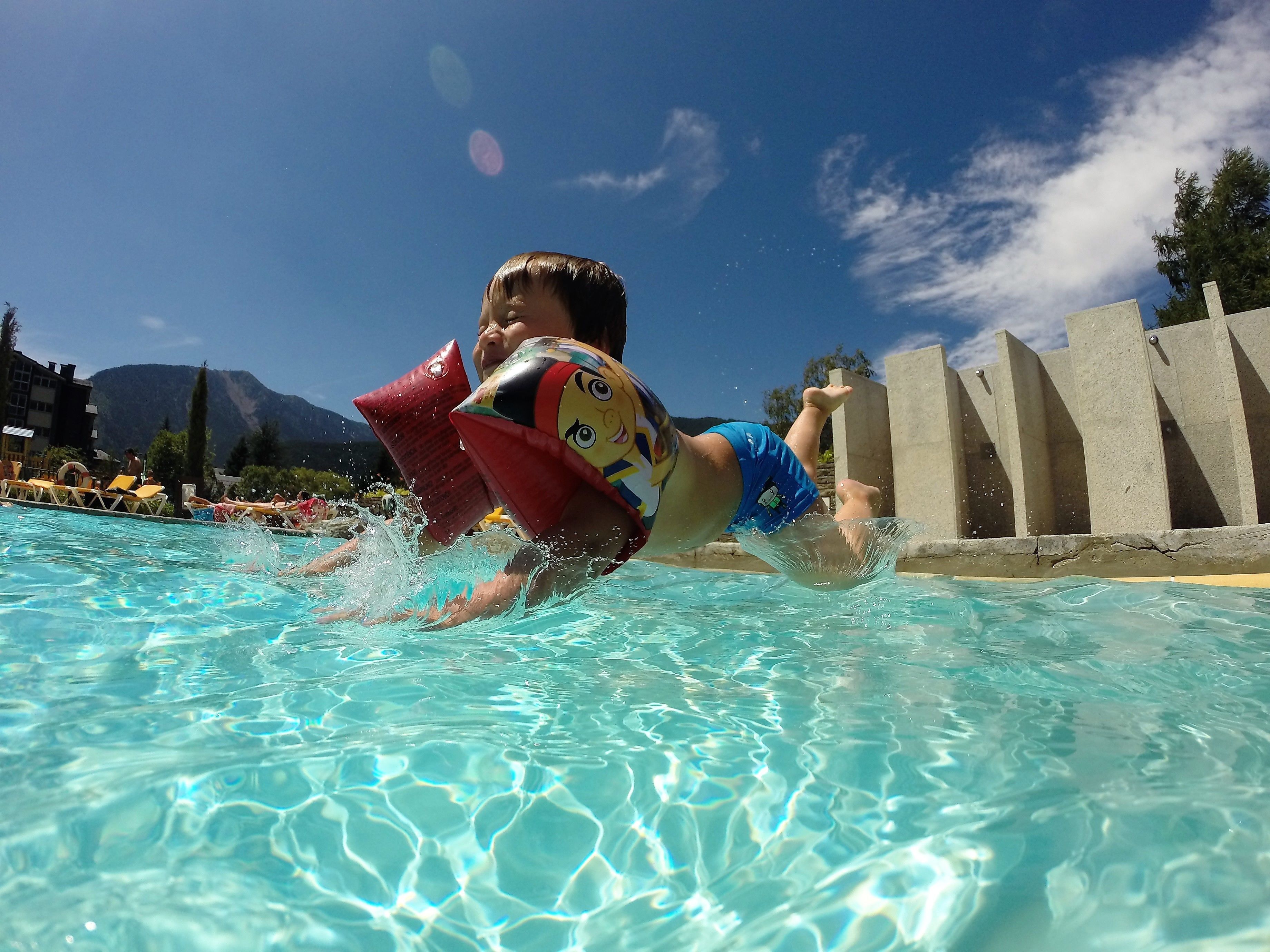 Una persona nadando en una piscina con agua cristalina, una torre de salvavidas y montañas al fondo.