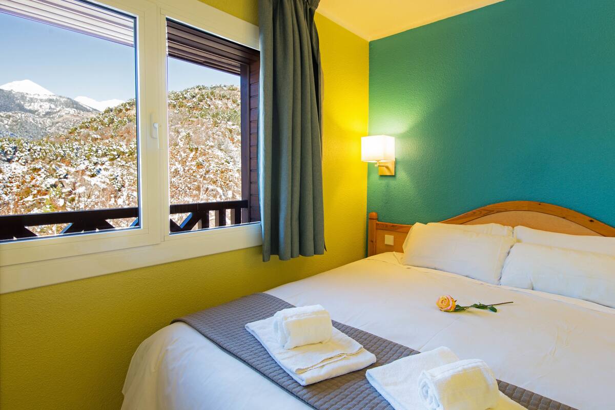 Quarto de hotel com uma cama, janela com vista para uma montanha nevada e parede verde.