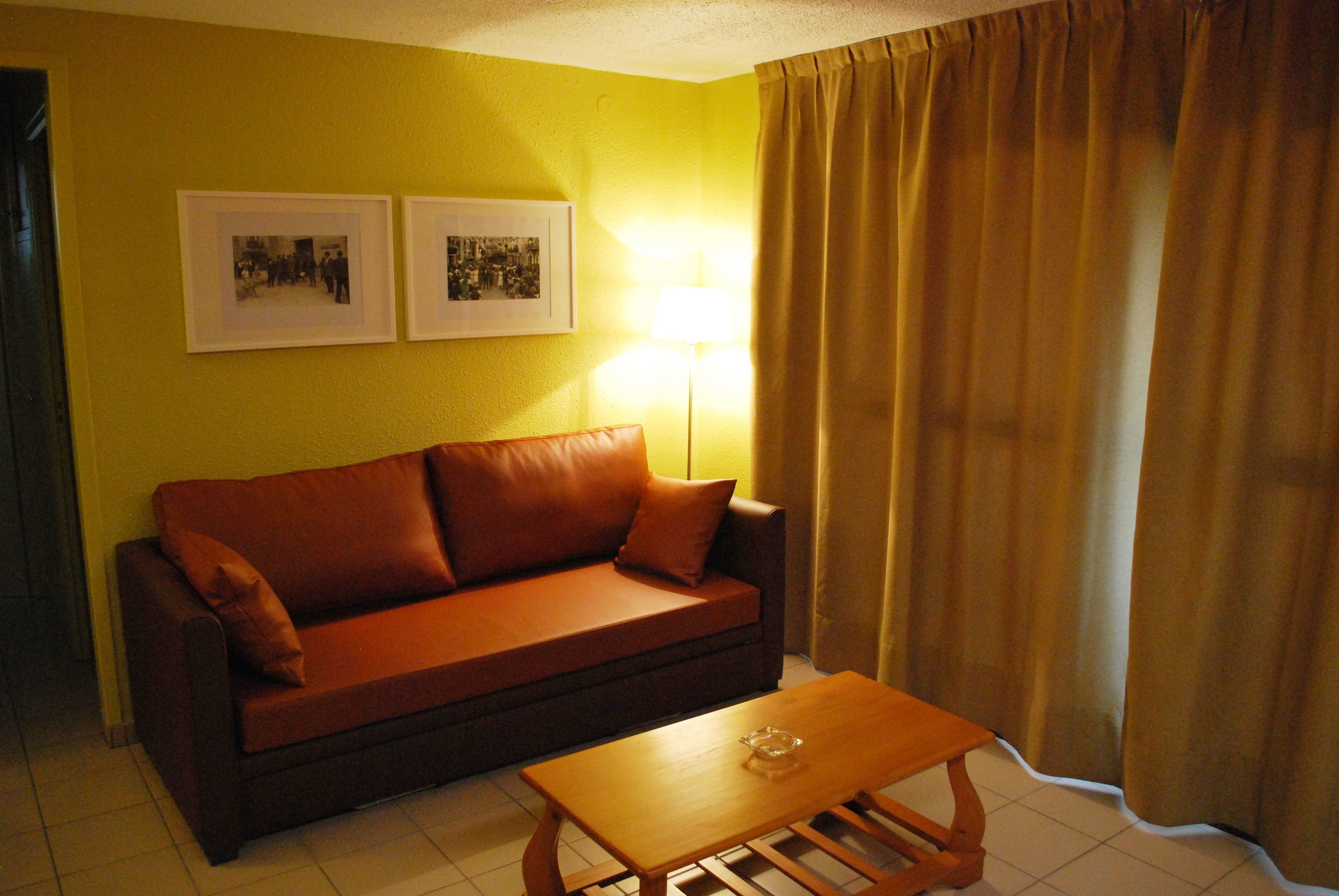 Una habitación con un sofá marrón, una mesa de centro de madera y dos cuadros en la pared.