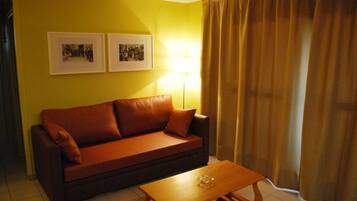 Una habitación con un sofá marrón, una mesa de centro de madera y dos cuadros en la pared.