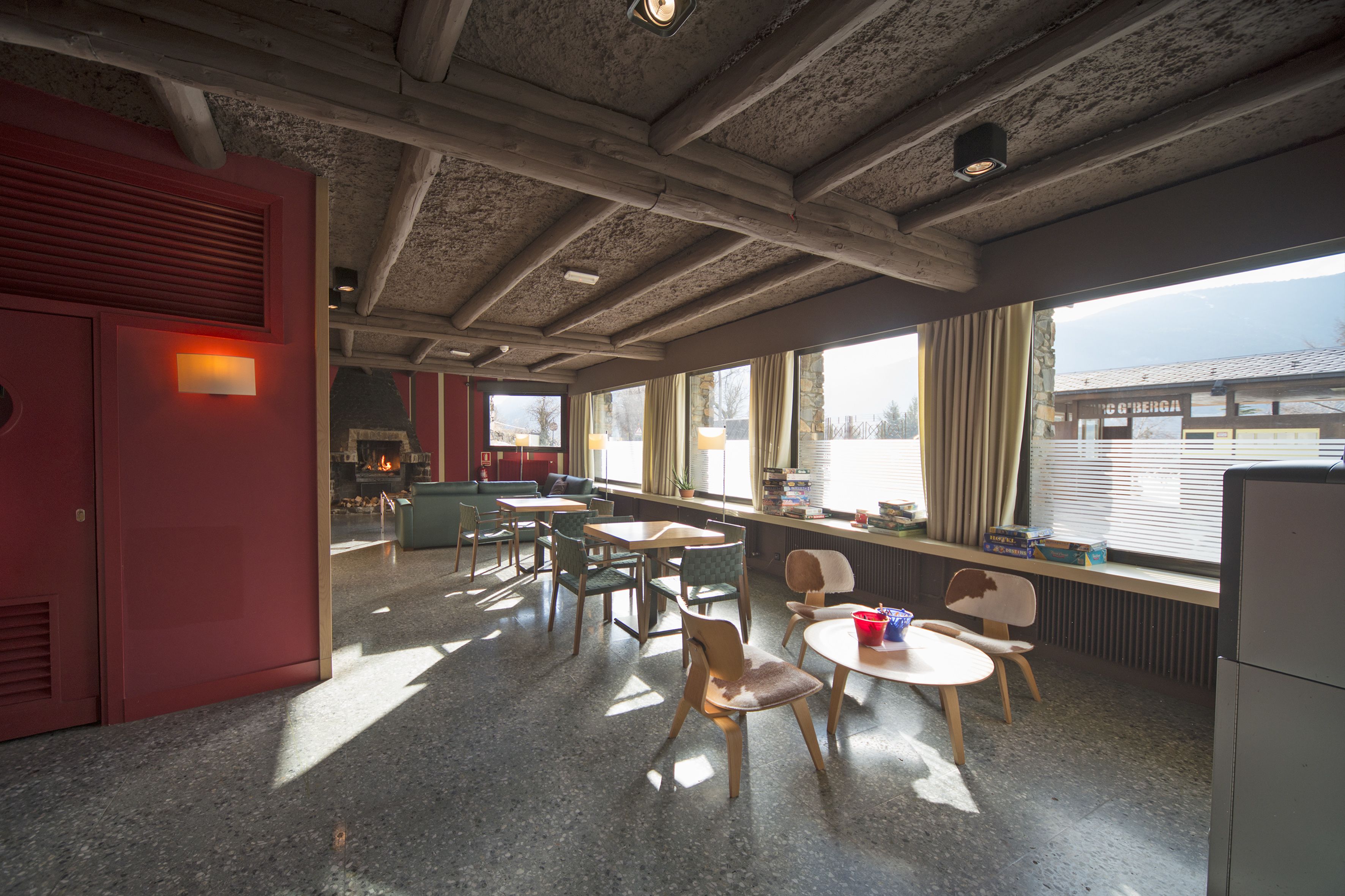 A spacious room with a high ceiling, large windows, and a mix of seating arrangements including tables and chairs.