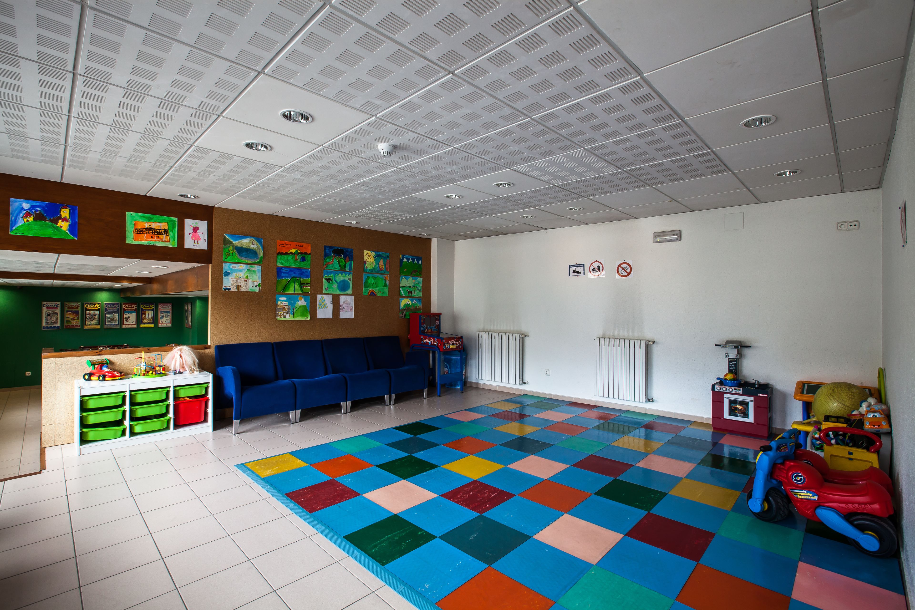 Un cuarto de juegos infantil con piso a cuadros de colores, asientos azules y varios juguetes.