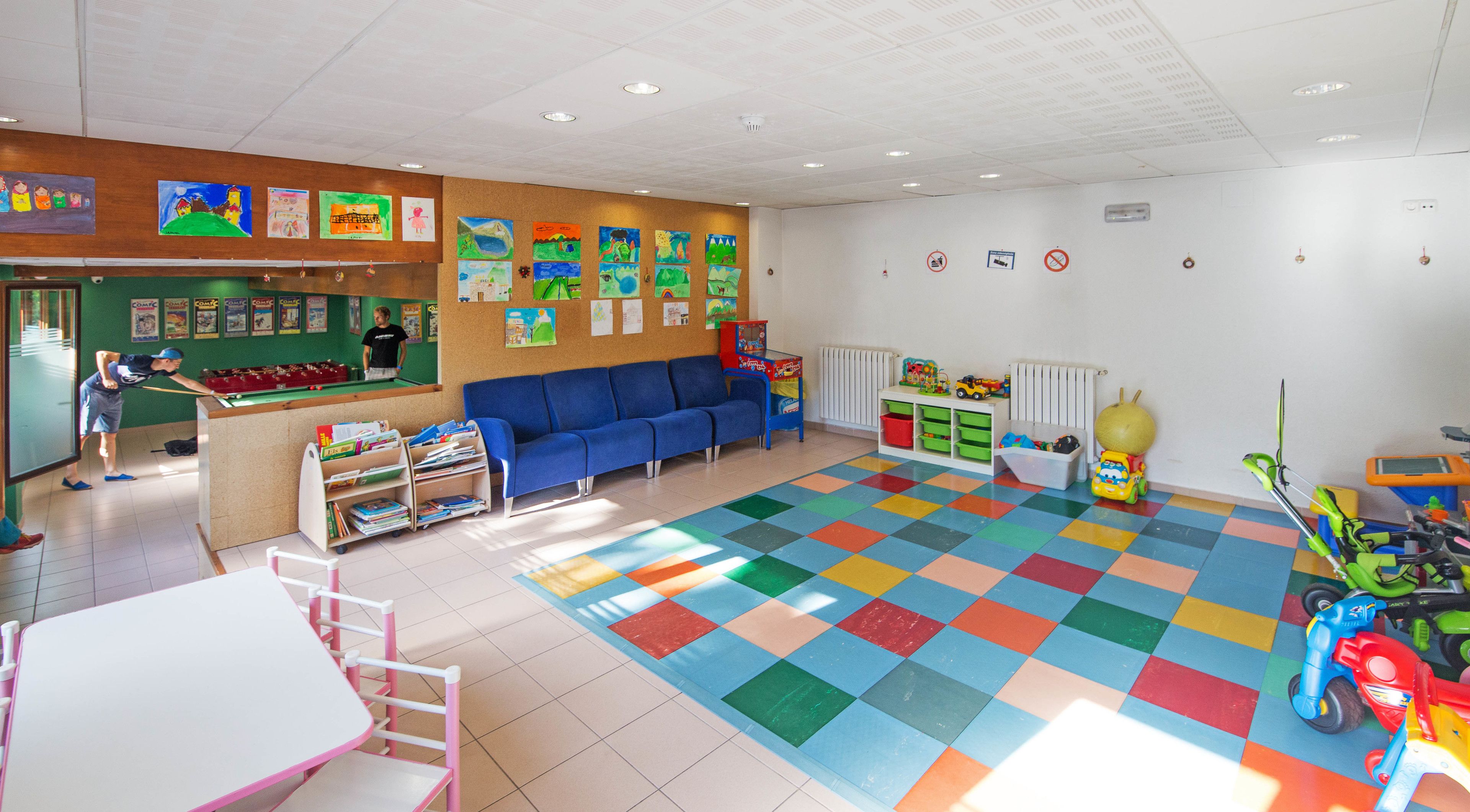 Una sala de juegos infantiles con billar, sofá azul, baldosas de colores y varios juguetes.