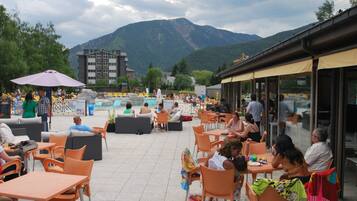 An outdoor seating area with tables and chairs, overlooking a pool and mountains.