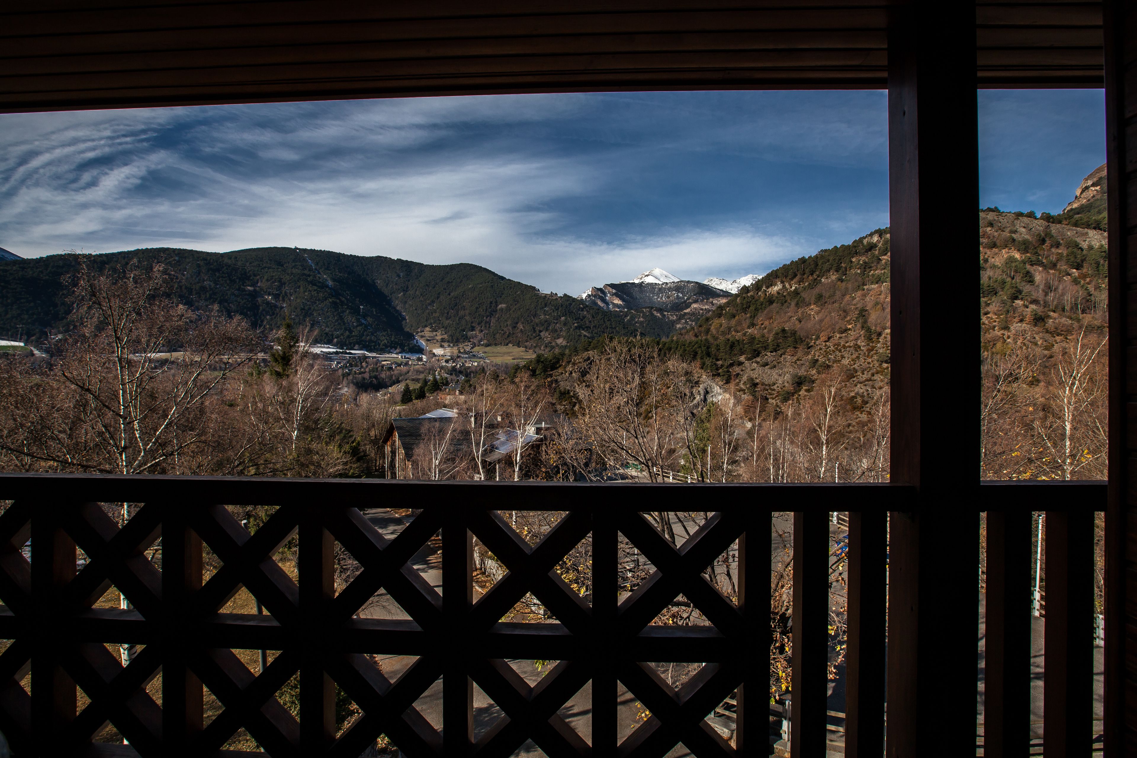 Vista desde un balcón con barandilla de celosía, sobre un valle con montañas y un pico nevado en la distancia.