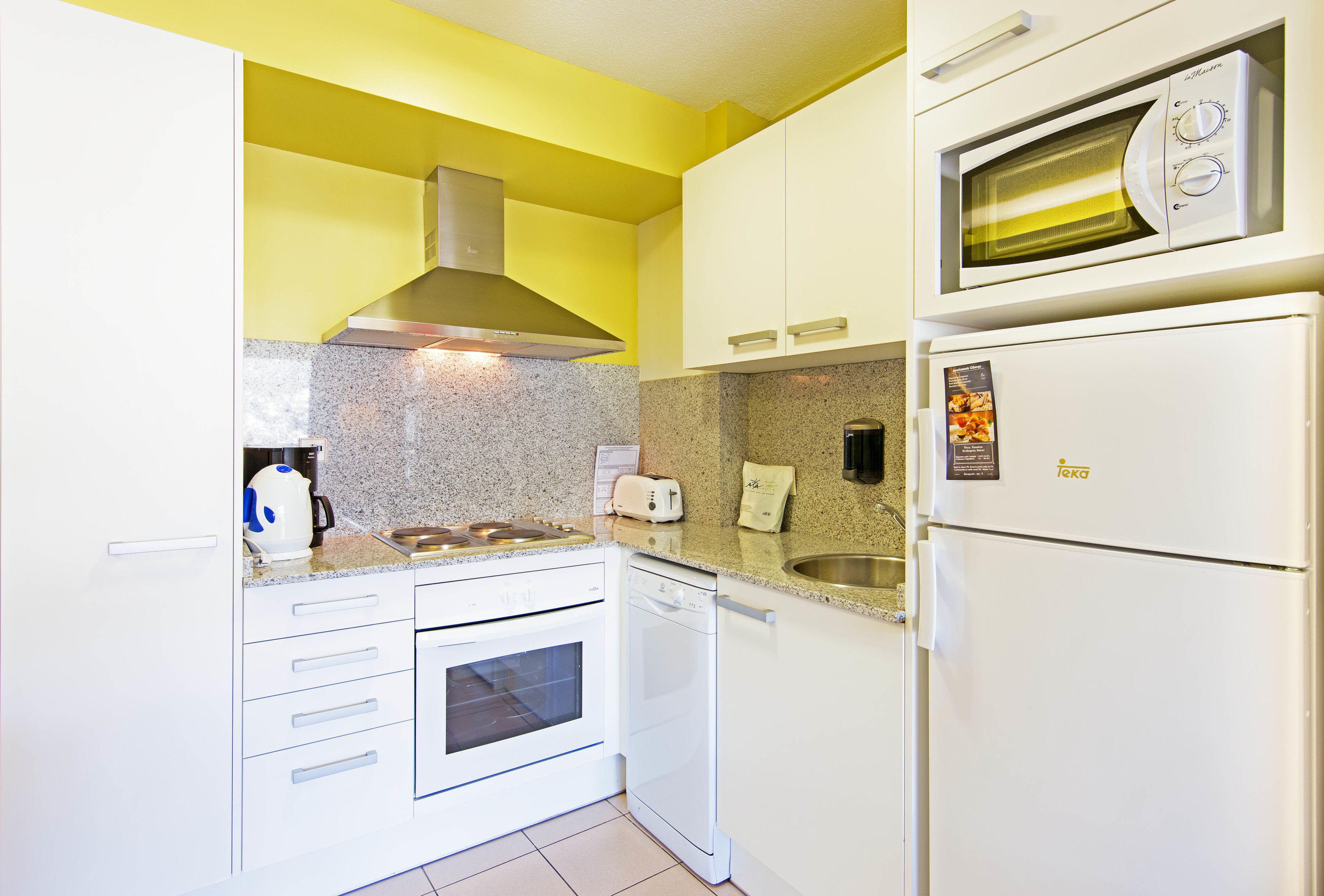 Una cocina compacta con armarios blancos, horno integrado, lavavajillas, microondas y tostadora.