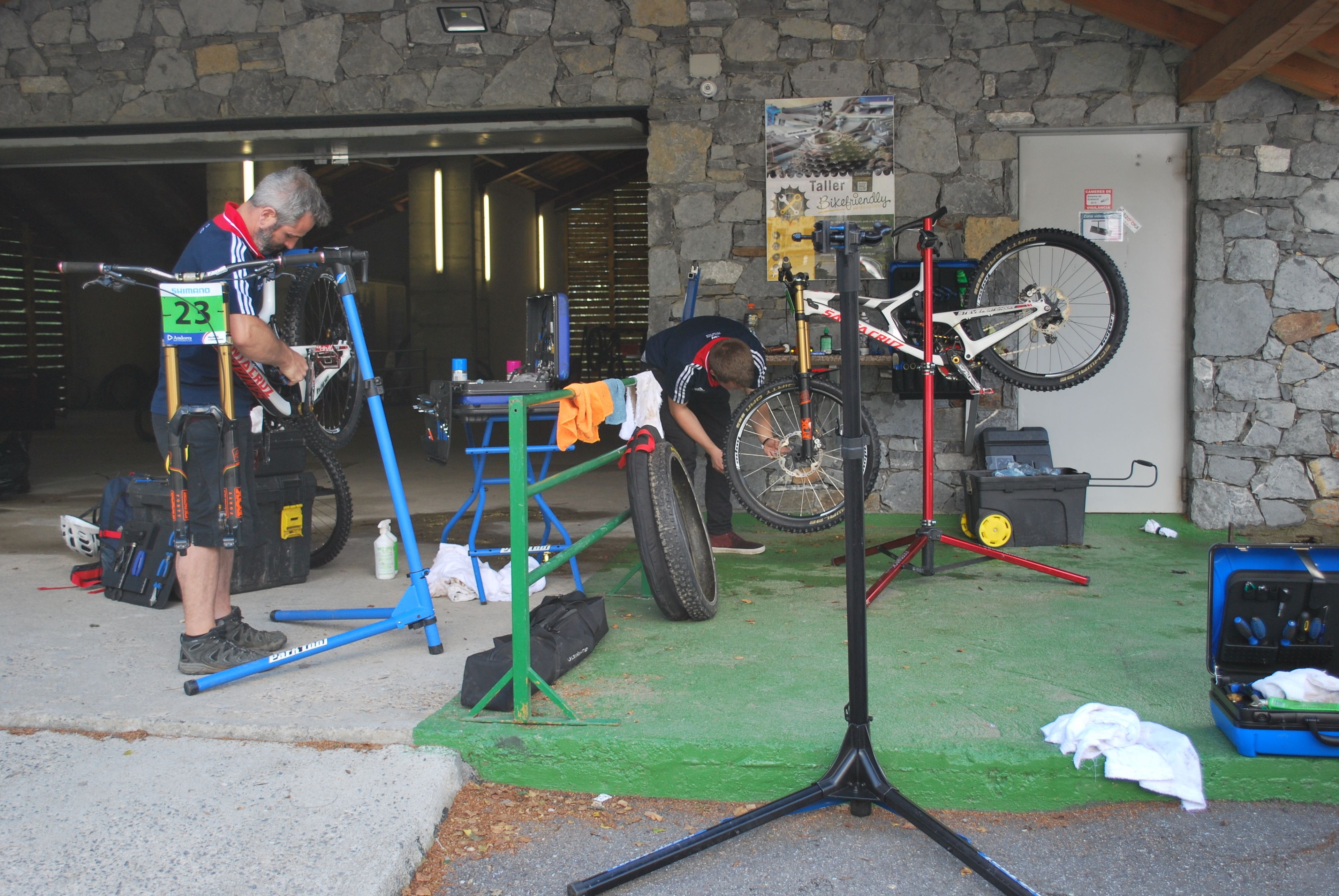 Un taller con bicicletas, herramientas, un muro de piedra y piso verde.