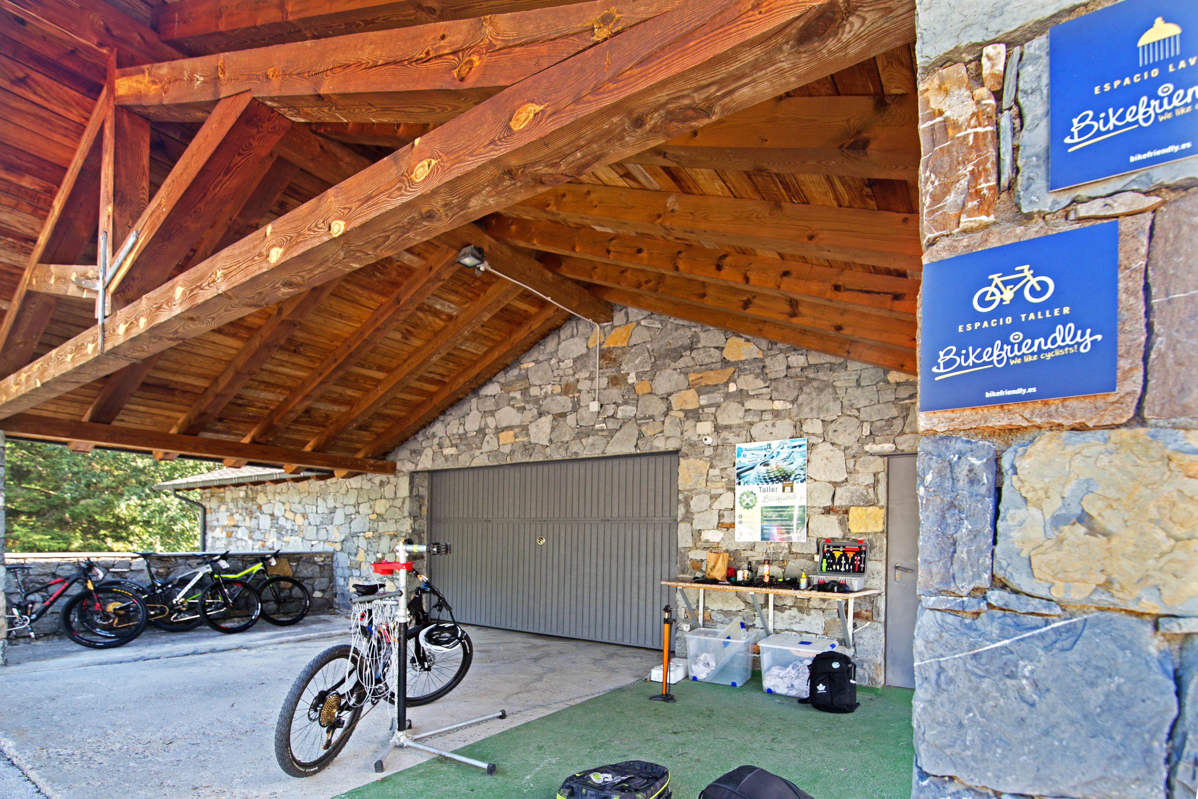 Un área de estacionamiento para bicicletas techada, con pared de piedra, vigas de madera y un cartel que indica un espacio amigable para ciclistas.