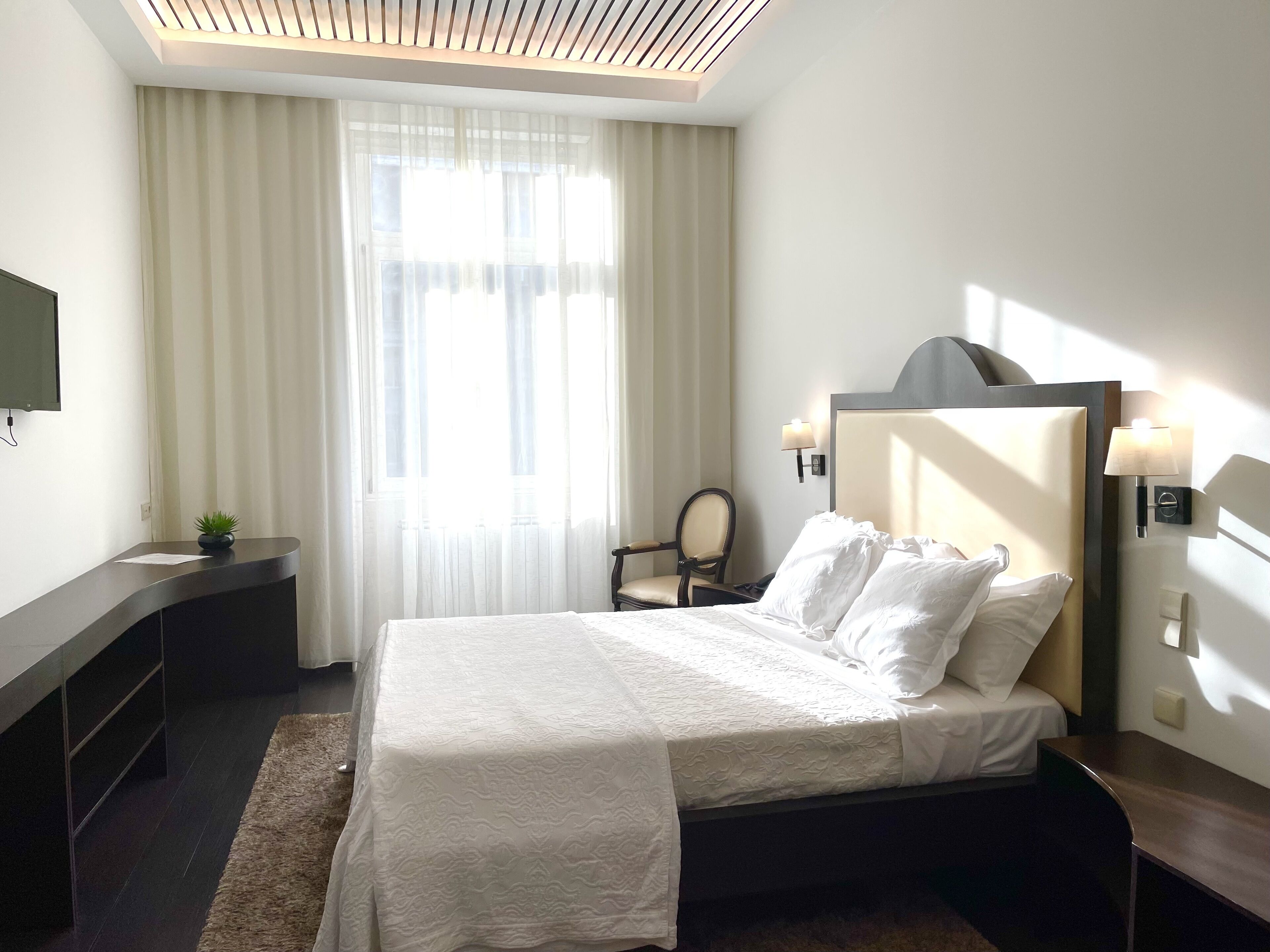 A hotel room with a bed, a desk, a chair, a TV, and a window with curtains.