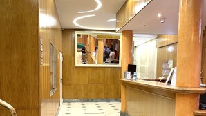 Un hall de hotel con un mostrador de recepción de madera, piso de baldosas y una escalera.
