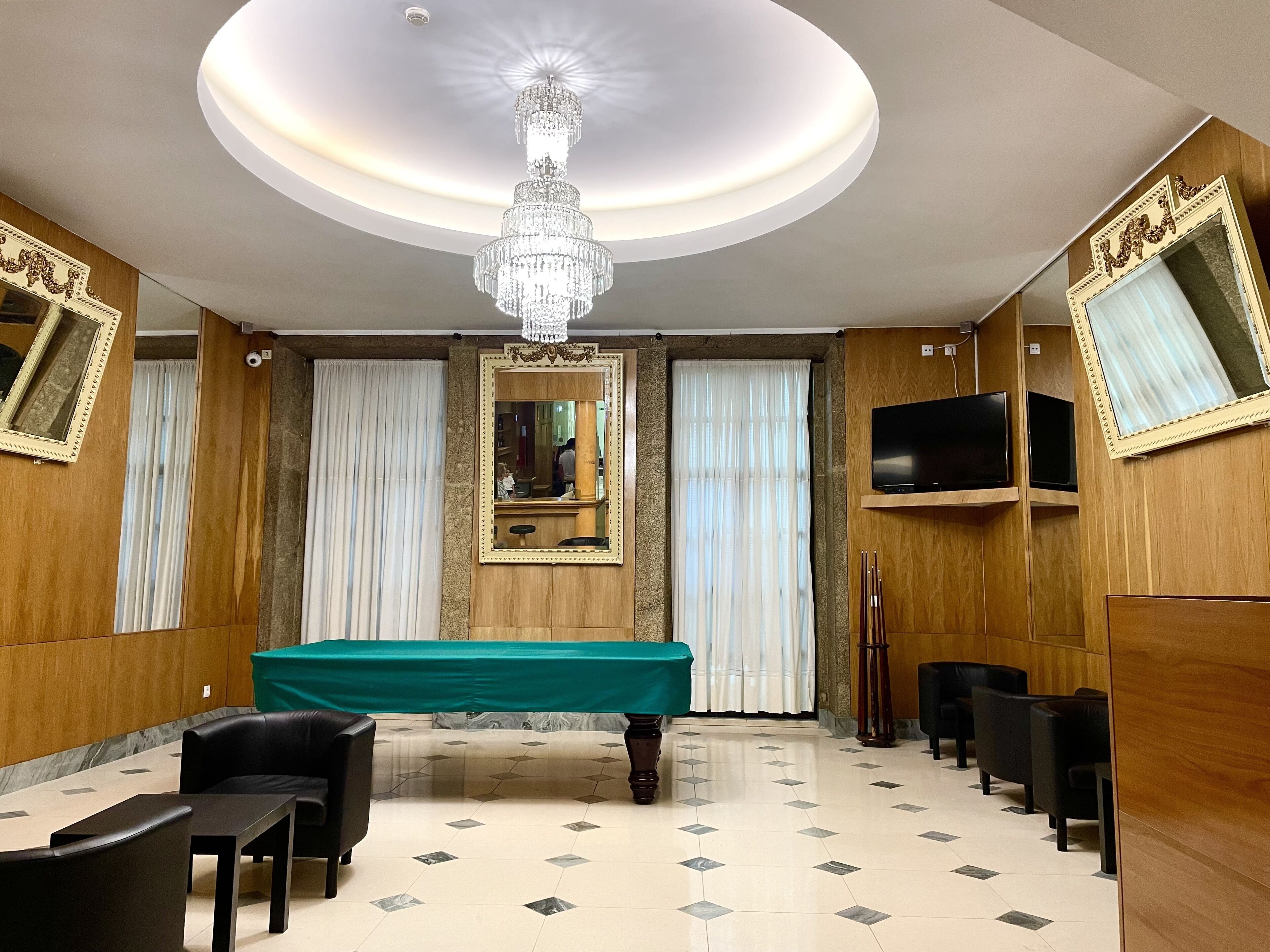Une pièce avec une table de billard, des fauteuils en cuir noir, un lustre et des boiseries.