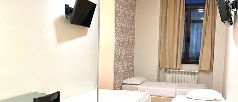 A room with two beds, a desk, a chair, a TV, and a window with curtains.