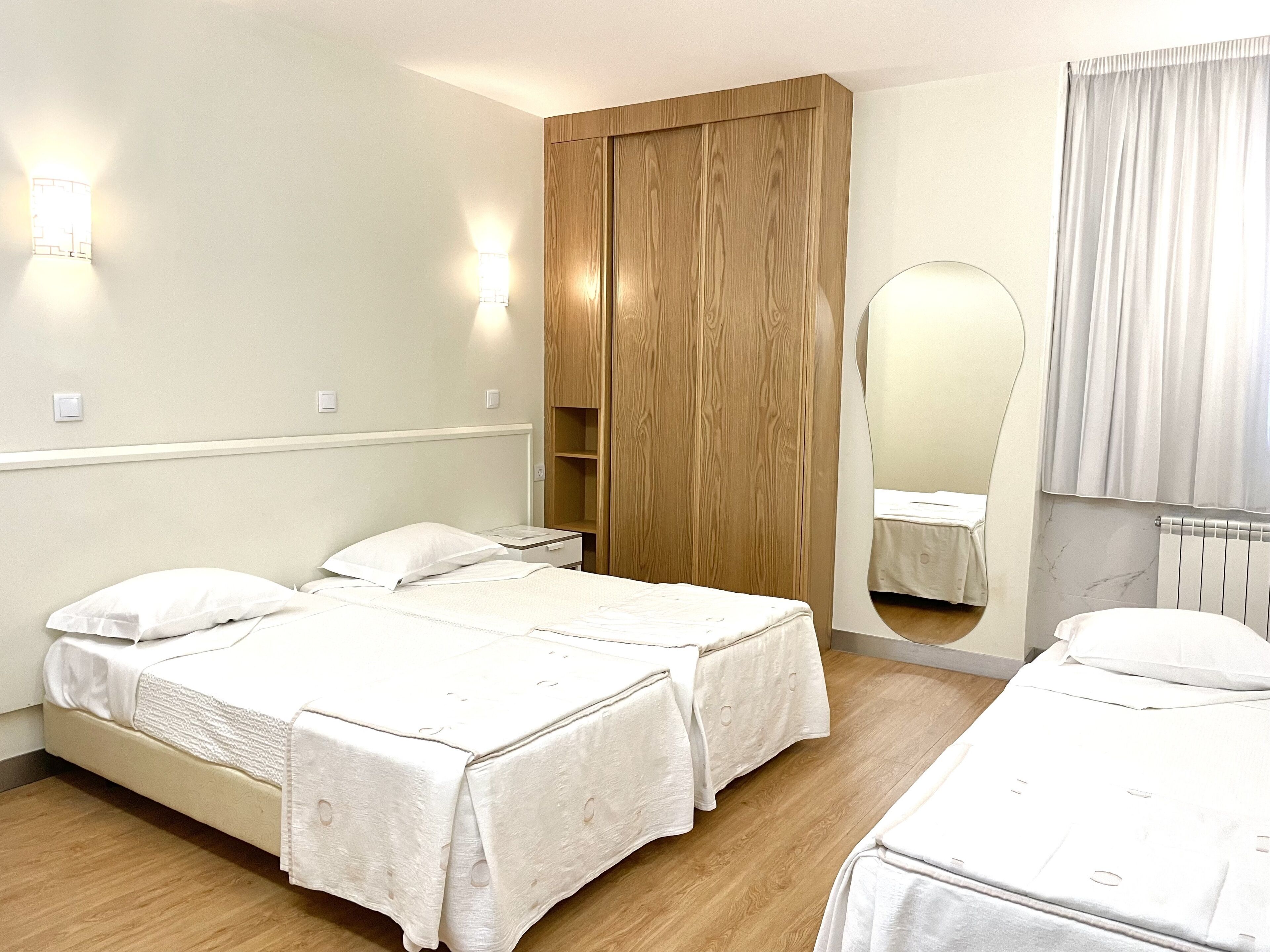 Quarto de hotel com duas camas, um guarda-roupa de madeira, um espelho e um radiador.