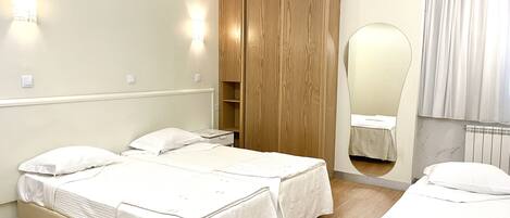 Quarto de hotel com duas camas, um guarda-roupa de madeira, um espelho e um radiador.