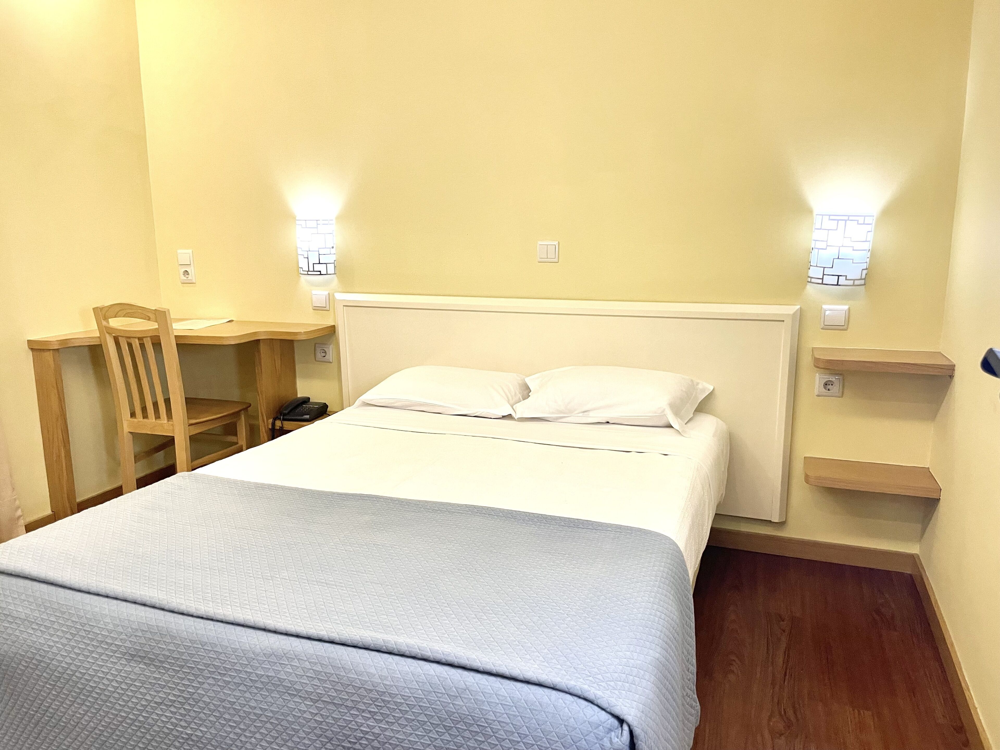 A hotel room with a bed, a desk, a chair, and a nightstand.