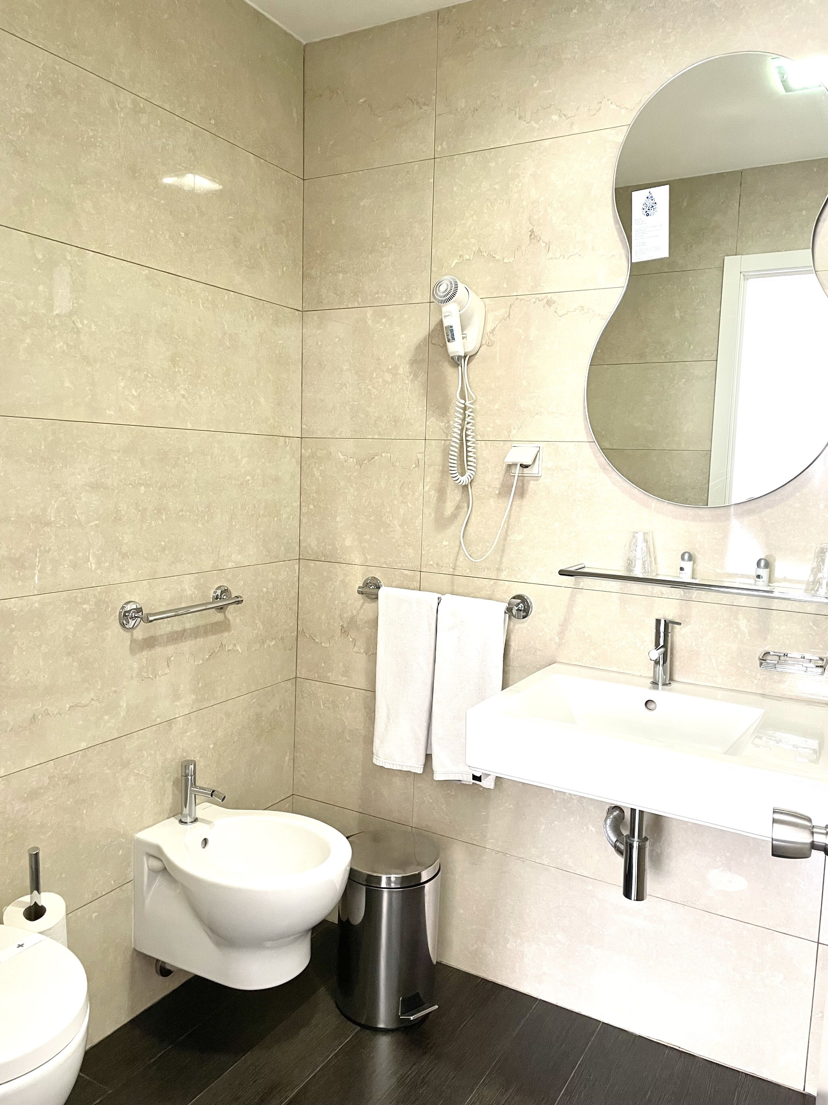 A modern bathroom with a bidet, toilet, sink, and a hairdryer mounted on the wall.