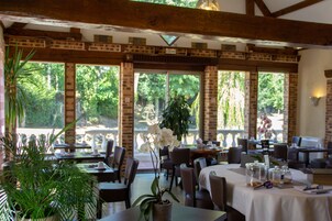 Un restaurante con paredes de ladrillo, amplias ventanas y plantas de interior. Las mesas están cubiertas con manteles blancos y presentan diferentes alimentos y aderezos.