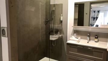 A modern bathroom with a glass-enclosed shower, a vanity with a mirror, and a sink.