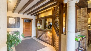 A reception area with a herringbone-patterned wall, a reception desk, a potted plant, and a column. - Oasis (Villaines-la-Juhel)