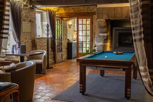 Una mesa de billar en una habitación con paredes de piedra, una chimenea y una vista por una puerta.