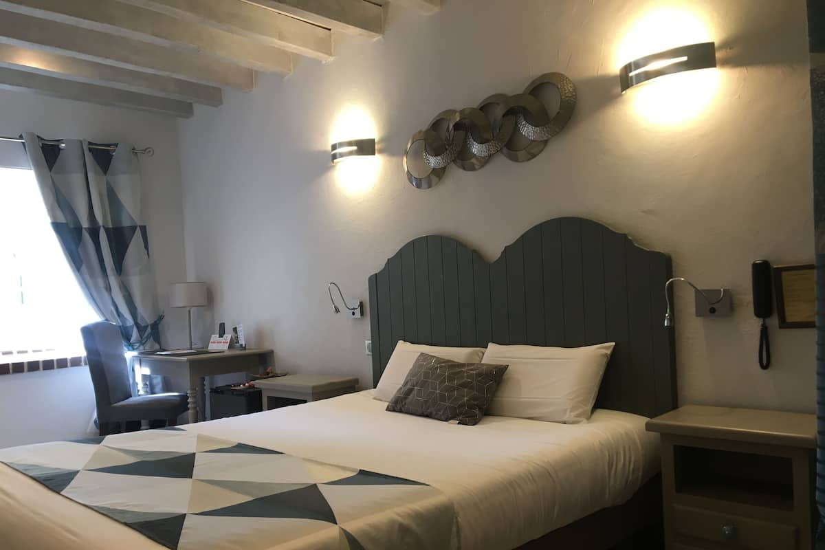 A hotel room with a large bed, bedside tables, a desk, and a wall-mounted phone.