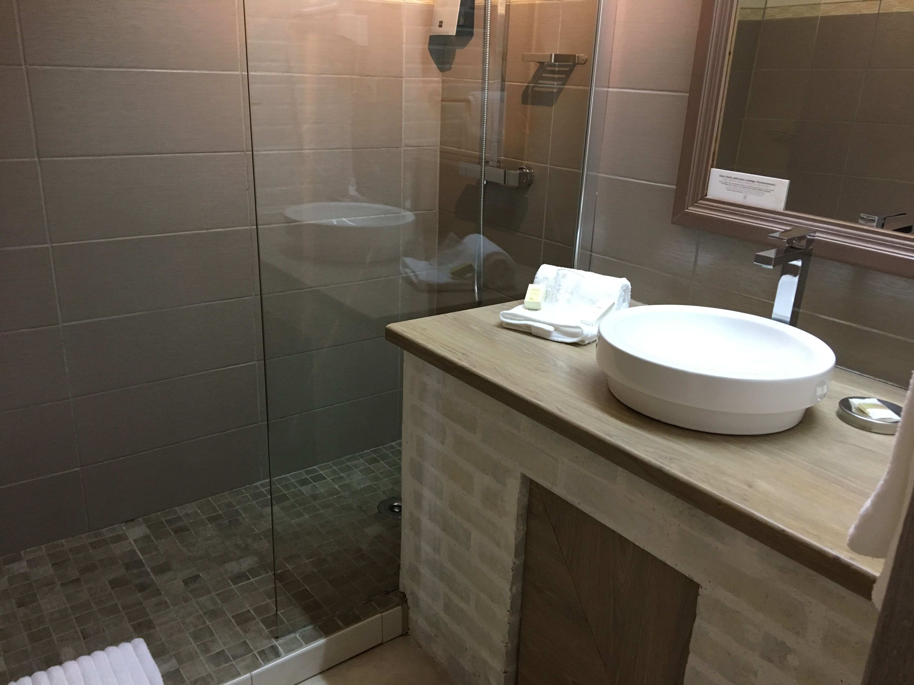 Ein modernes Badezimmer mit einer Duschkabine, einem runden Waschbecken und einem Spiegel darüber.