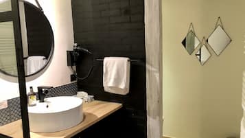 Un bagno con uno specchio rotondo, un lavandino bianco, un portascopevoli e una parete di mattoni neri.