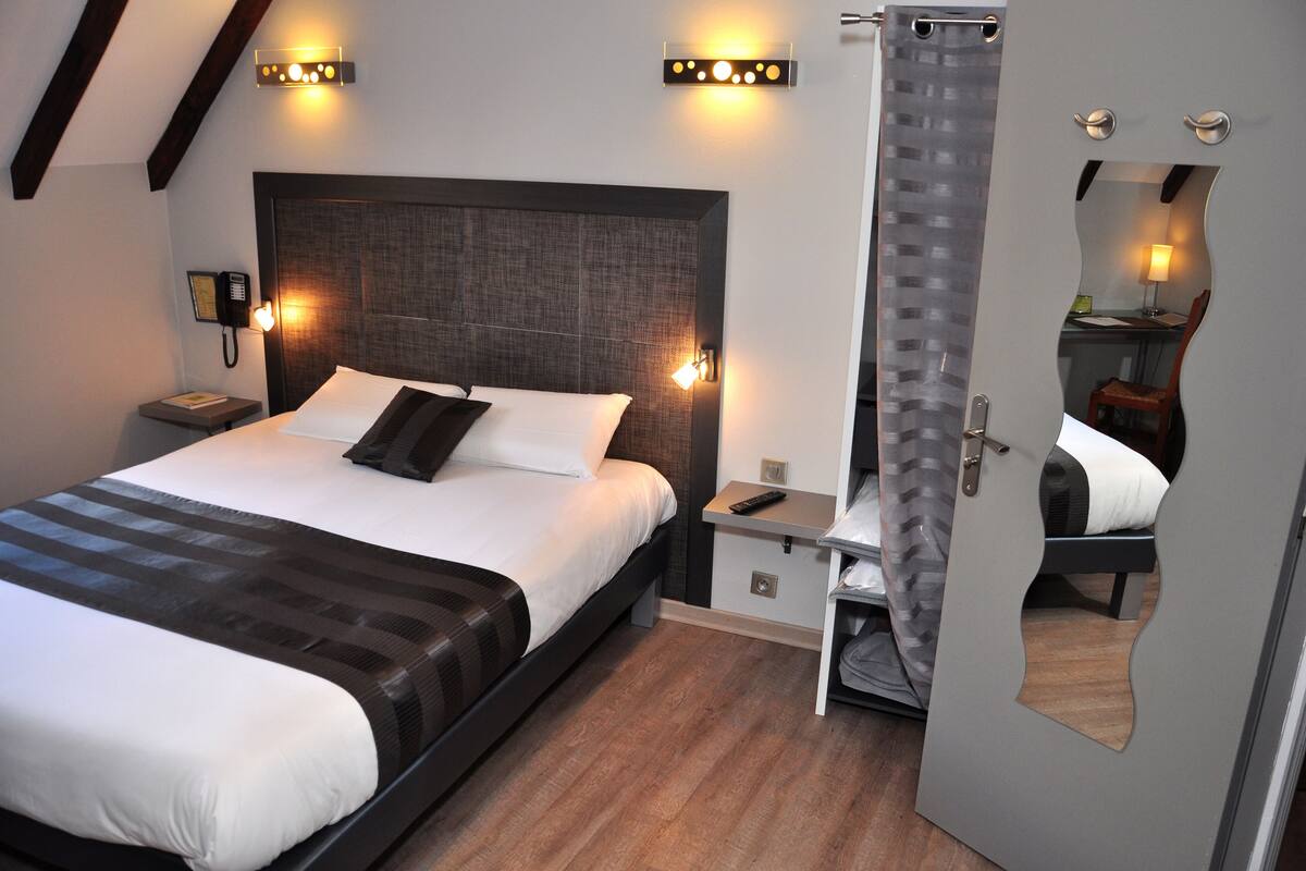 A modern hotel room with a large bed, bedside tables, a phone, and a mirror.