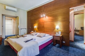 Una habitación de hotel con cabecera de madera, dos lámparas de noche, una cama con colcha, una mesita de noche y un armario.
