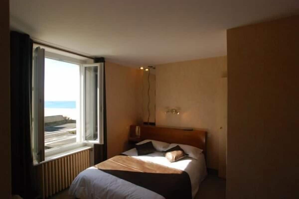 A hotel room with a bed, a window with curtains, a bedside table, and a nightstand.