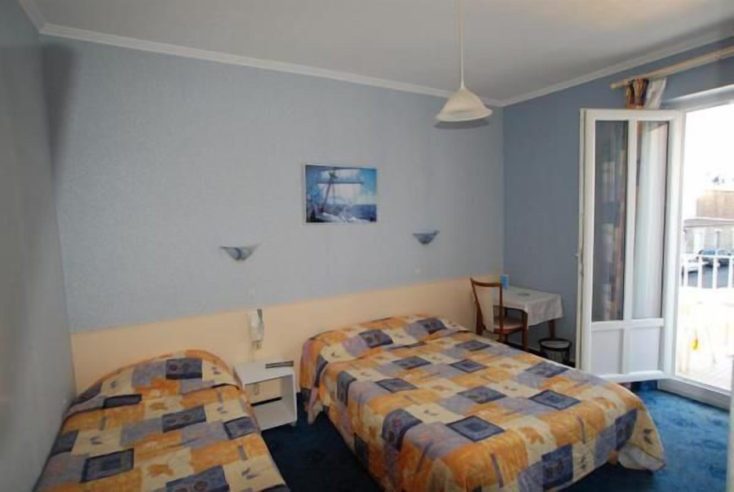 A hotel room with two beds, a small desk, a chair, a painting on the wall, and a sliding door to the outside.