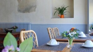A dining area with a wooden table set for two, surrounded by wicker chairs. A potted plant is visible on the wall above the table. - Hotel Alpha Océan (Saint-Malo)