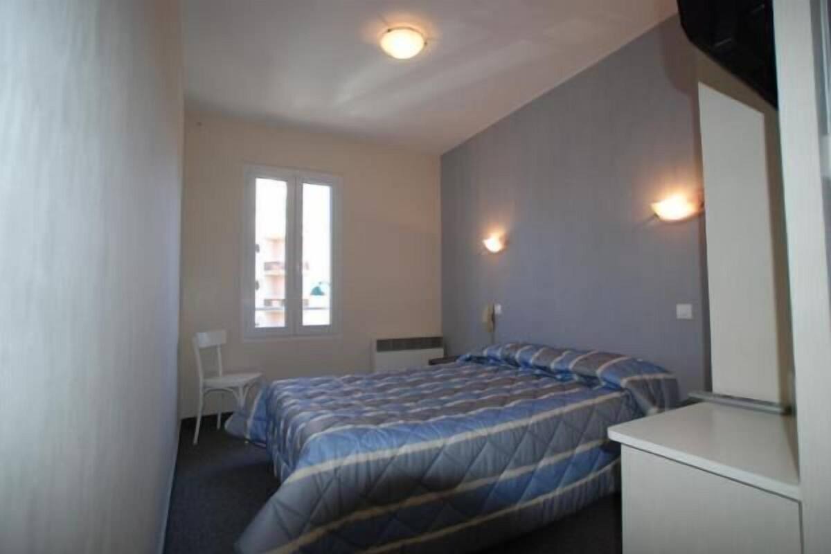 A bedroom with a bed, a desk, a chair, and a window.