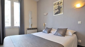 Habitación de hotel con una cama grande, una ventana con cortinas, una lámpara de pared y un cuadro.