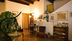 A cozy living room with a wooden ceiling, a dining area with a table and chairs, and a bookshelf filled with books and magazines. - Mondo Antico Alloggio in Città B&B (Cesena)