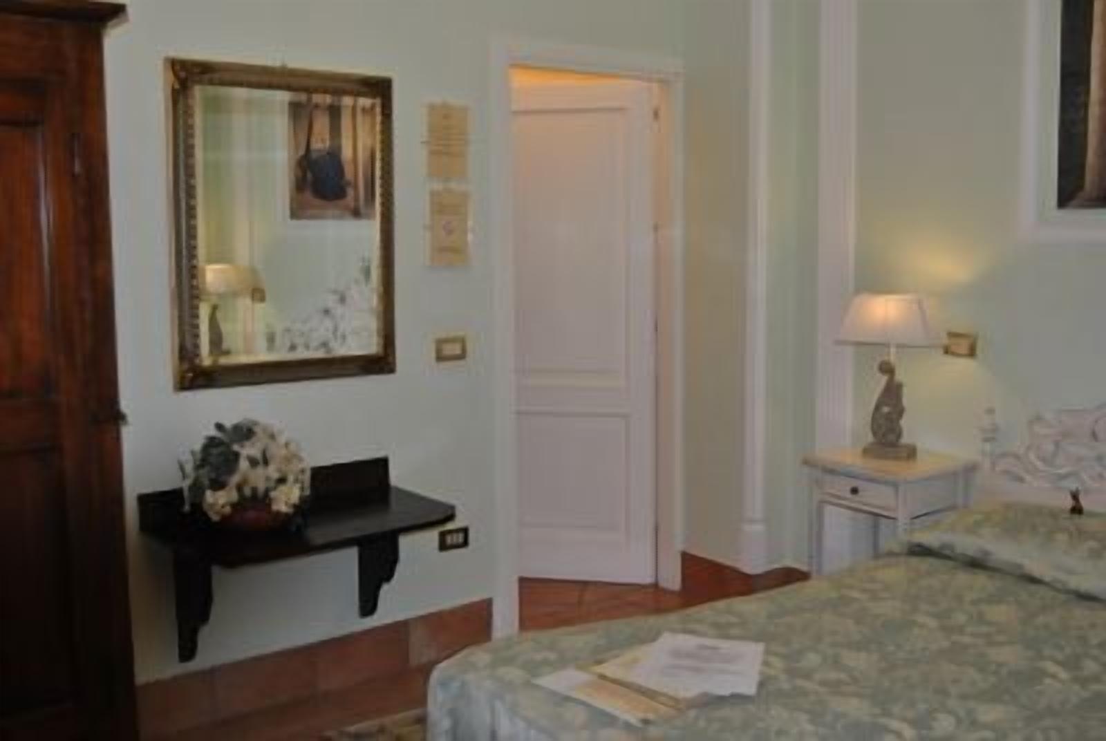 Una habitación de hotel con cama, mesita de noche, escritorio, espejo y puerta.