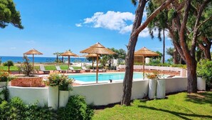 A pool area with umbrellas, lounge chairs, and a view of the ocean. - Hotel Mare Pineta (Pula)