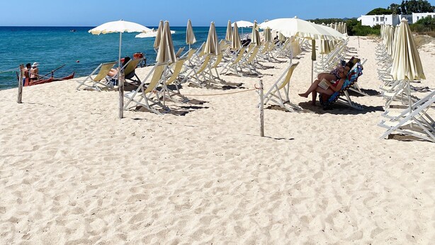 A beach with rows of sun loungers and umbrellas, a clear blue sky, and the sea in the background. - Hotel Mare Pineta (Pula)