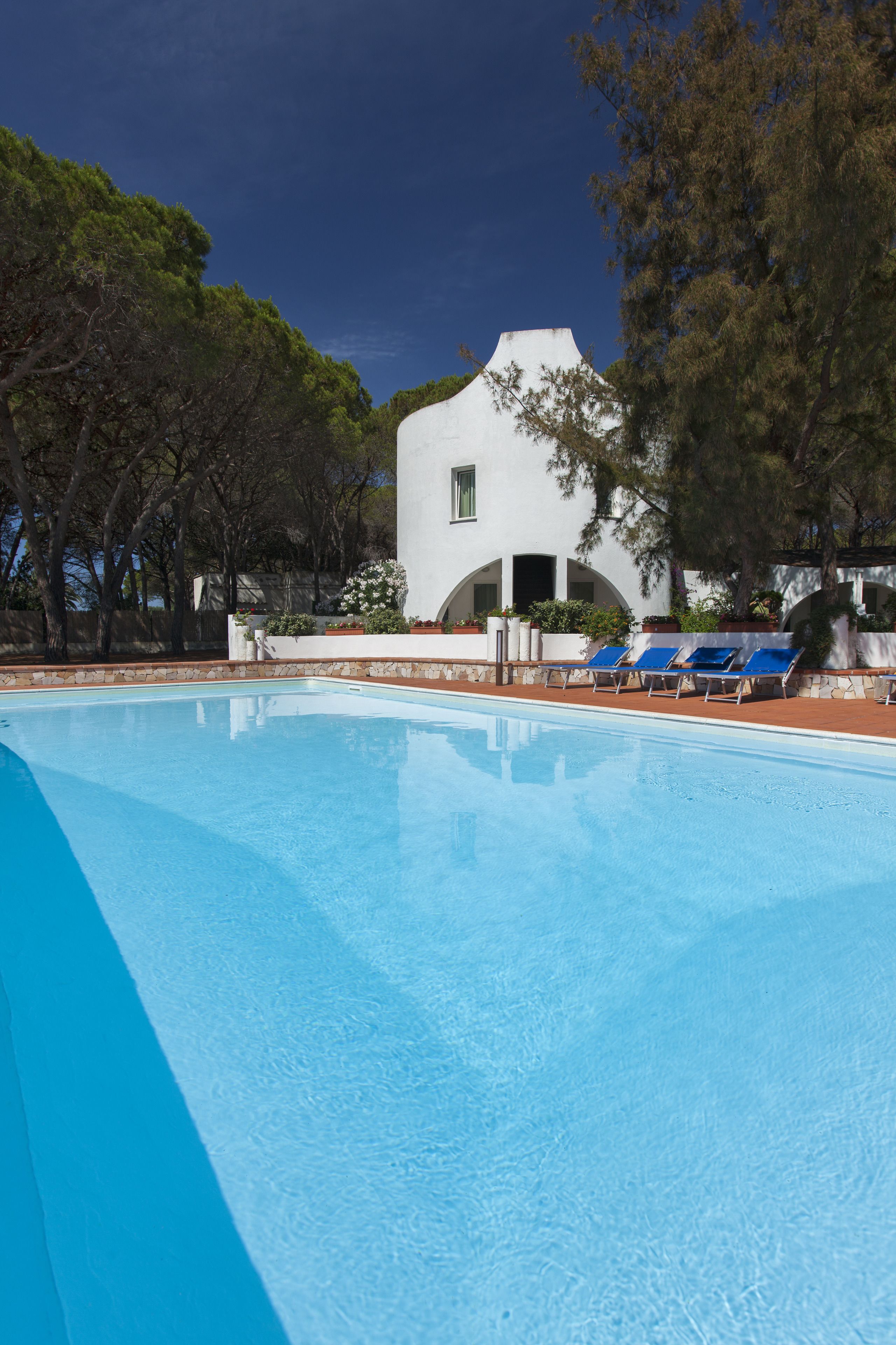 Ein Swimmingpool mit blauem Wasser, umgeben von Liegestühlen und einem weißen Gebäude mit Bogenfenstern.
