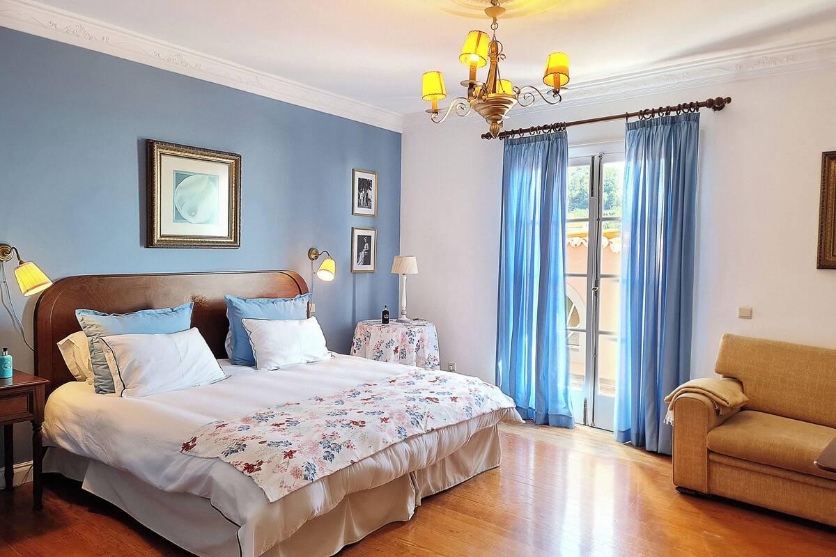 Un dormitorio con cama, mesitas de noche, candelabro, sofá y vistas al exterior.